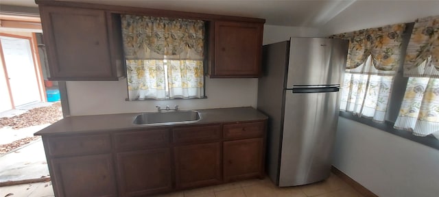 kitchen with light tile patterned floors, vaulted ceiling, stainless steel refrigerator, and sink