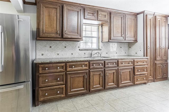 kitchen featuring light tile patterned flooring, light stone counters, sink, and stainless steel refrigerator