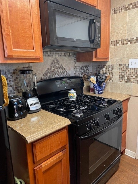 kitchen with black appliances, hardwood / wood-style floors, and tasteful backsplash