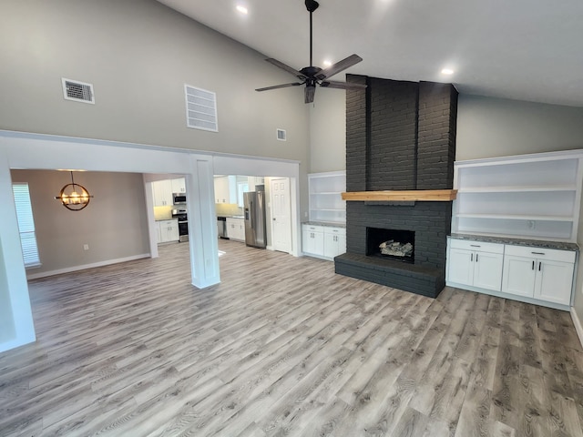 unfurnished living room featuring a fireplace, ceiling fan with notable chandelier, light hardwood / wood-style flooring, and high vaulted ceiling