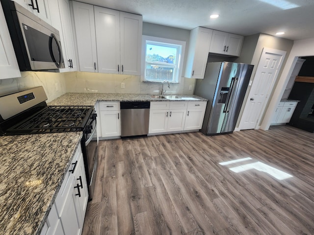 kitchen with appliances with stainless steel finishes, light wood-type flooring, sink, stone countertops, and white cabinets