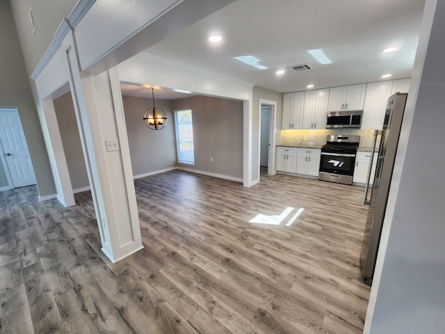 kitchen featuring backsplash, light hardwood / wood-style flooring, appliances with stainless steel finishes, a notable chandelier, and white cabinetry