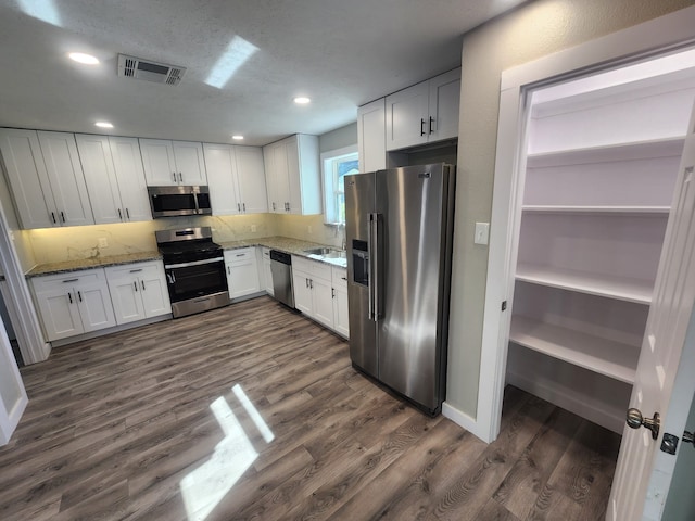 kitchen with dark hardwood / wood-style flooring, dark stone counters, decorative backsplash, white cabinets, and appliances with stainless steel finishes