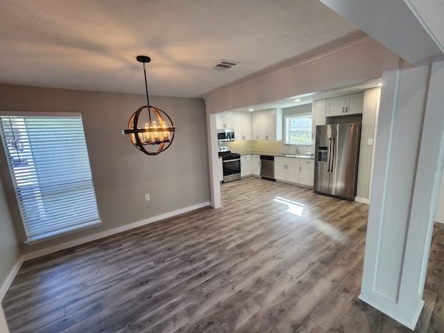 kitchen featuring hanging light fixtures, appliances with stainless steel finishes, a chandelier, white cabinets, and hardwood / wood-style flooring