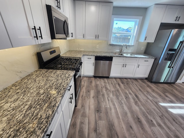 kitchen with light stone countertops, appliances with stainless steel finishes, light hardwood / wood-style floors, and white cabinetry