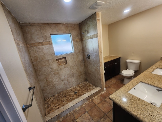 bathroom with tiled shower, a textured ceiling, vanity, and toilet