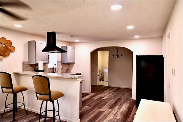 kitchen with a breakfast bar area, island range hood, dark wood-type flooring, and kitchen peninsula