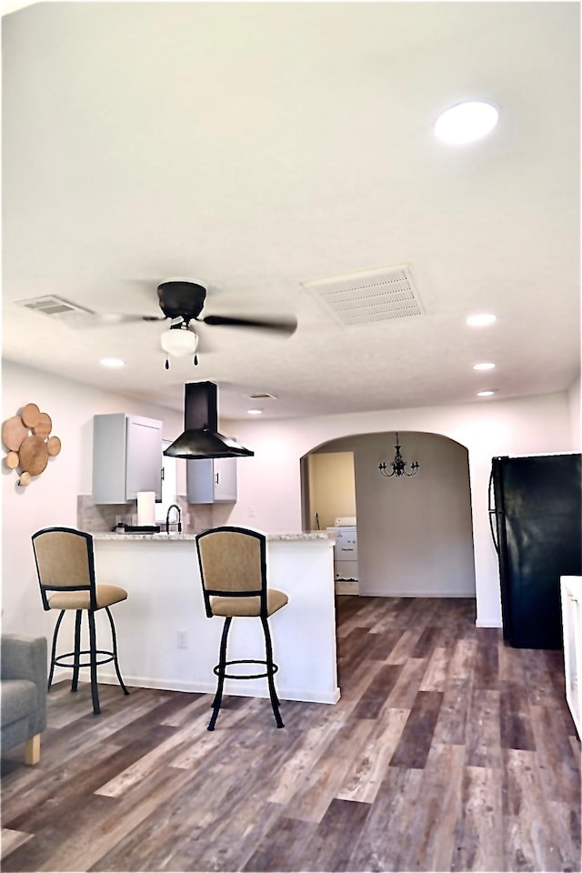 kitchen with sink, island exhaust hood, black fridge, dark hardwood / wood-style flooring, and kitchen peninsula