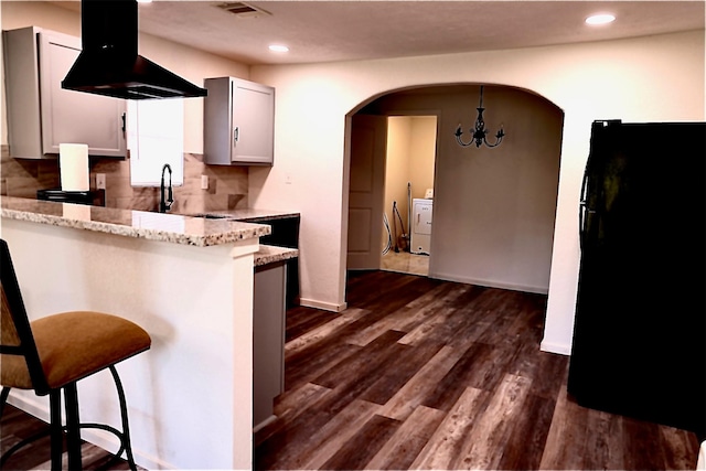 kitchen featuring island range hood, white cabinetry, a kitchen breakfast bar, light stone countertops, and dark wood-type flooring