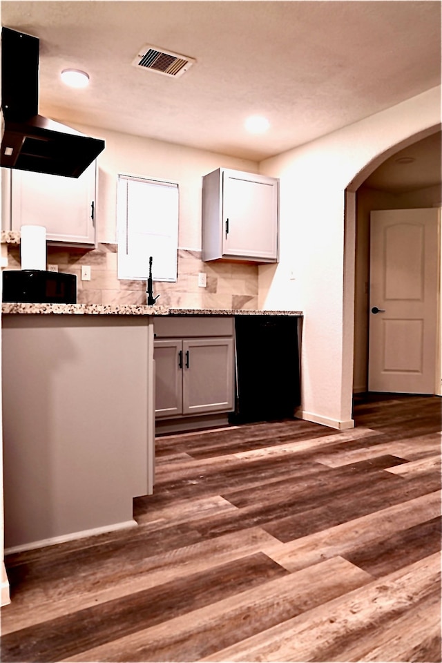 kitchen featuring exhaust hood, decorative backsplash, light stone countertops, dark hardwood / wood-style flooring, and white cabinetry