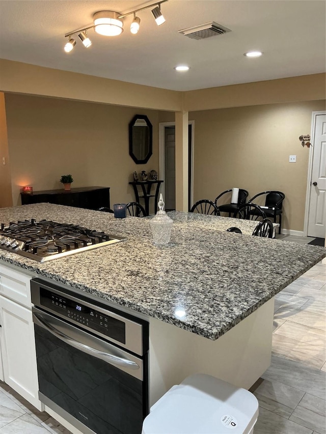 kitchen featuring appliances with stainless steel finishes, white cabinetry, visible vents, and dark stone countertops