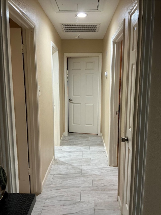 hall with attic access, visible vents, and baseboards