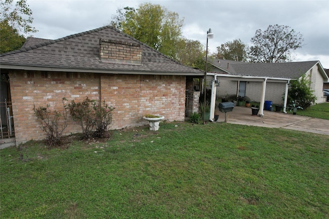 exterior space featuring roof with shingles, brick siding, a lawn, and a patio area