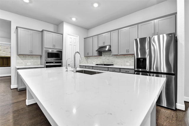 kitchen featuring a spacious island, sink, dark hardwood / wood-style floors, decorative backsplash, and appliances with stainless steel finishes