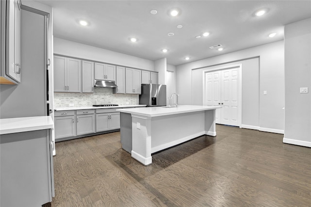 kitchen with gray cabinetry, black gas cooktop, dark hardwood / wood-style floors, an island with sink, and stainless steel fridge with ice dispenser