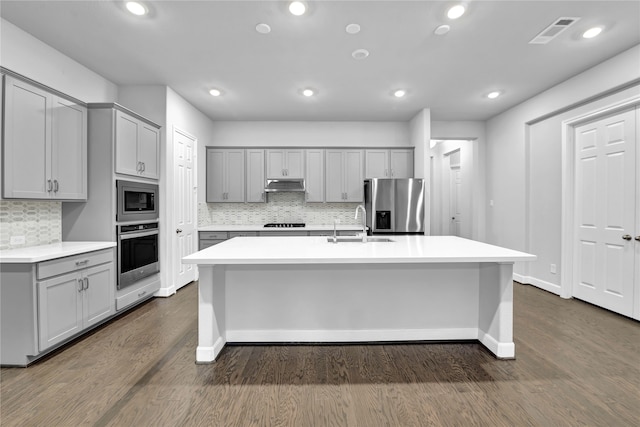 kitchen featuring stainless steel appliances, dark hardwood / wood-style floors, gray cabinetry, and a kitchen island with sink