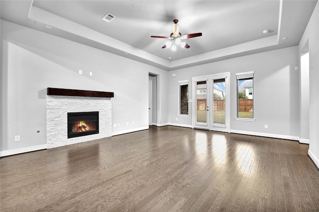 unfurnished living room with ceiling fan, a stone fireplace, dark wood-type flooring, and a tray ceiling