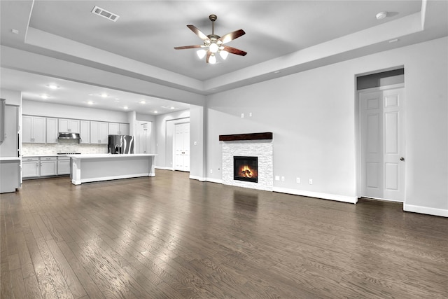 unfurnished living room with ceiling fan, dark hardwood / wood-style flooring, a fireplace, and a tray ceiling