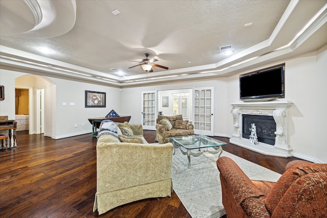 living room featuring a high end fireplace, a textured ceiling, a raised ceiling, ceiling fan, and dark hardwood / wood-style floors