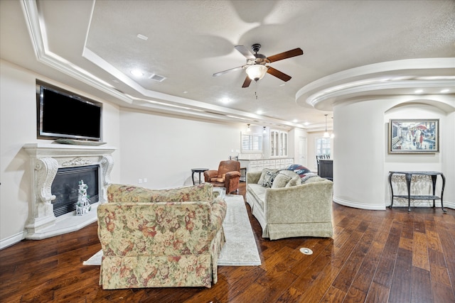 living room with crown molding, ceiling fan, a textured ceiling, a fireplace, and dark hardwood / wood-style flooring