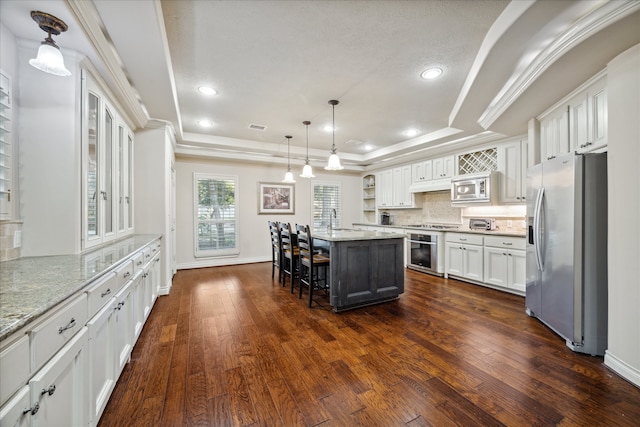 kitchen featuring a breakfast bar, a center island, white cabinets, a raised ceiling, and appliances with stainless steel finishes