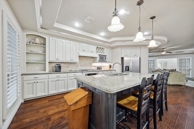 kitchen featuring stainless steel appliances, a tray ceiling, dark wood-type flooring, sink, and white cabinetry