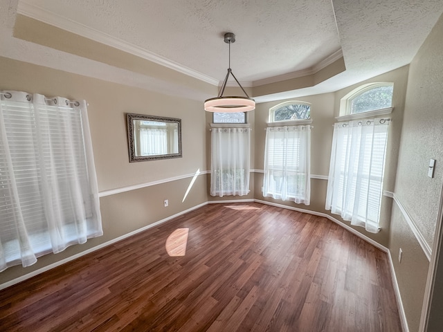 unfurnished dining area with a textured ceiling, hardwood / wood-style flooring, crown molding, and a tray ceiling