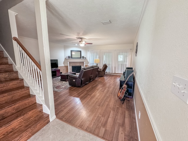 living room with ceiling fan, light wood-type flooring, a textured ceiling, and ornamental molding