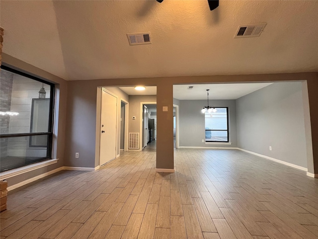 empty room with light hardwood / wood-style floors, a textured ceiling, and an inviting chandelier