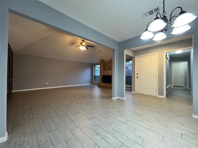 unfurnished living room featuring ceiling fan with notable chandelier, light wood-type flooring, a brick fireplace, and lofted ceiling