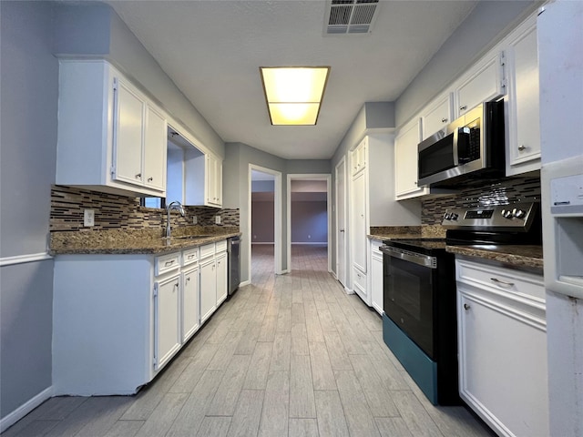 kitchen with appliances with stainless steel finishes, backsplash, white cabinetry, and dark stone counters