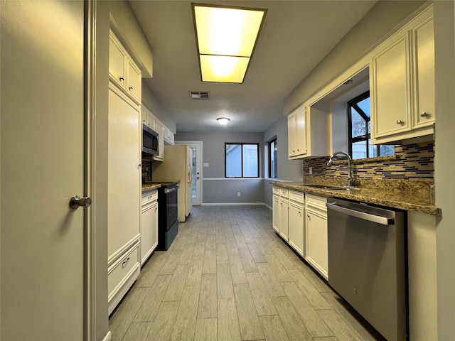 kitchen featuring sink, dark stone countertops, light hardwood / wood-style floors, white cabinets, and appliances with stainless steel finishes