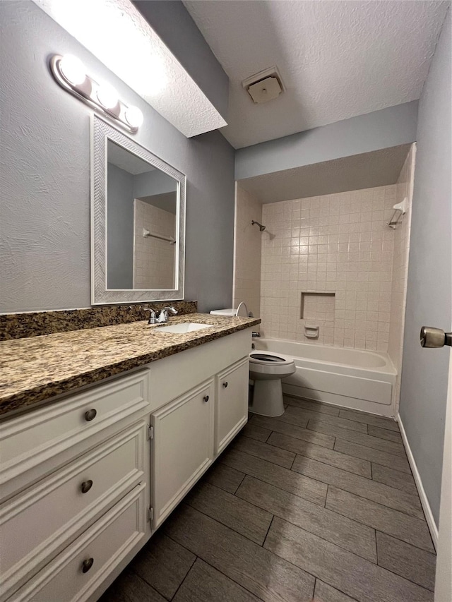 full bathroom with a textured ceiling, vanity, toilet, and tiled shower / bath