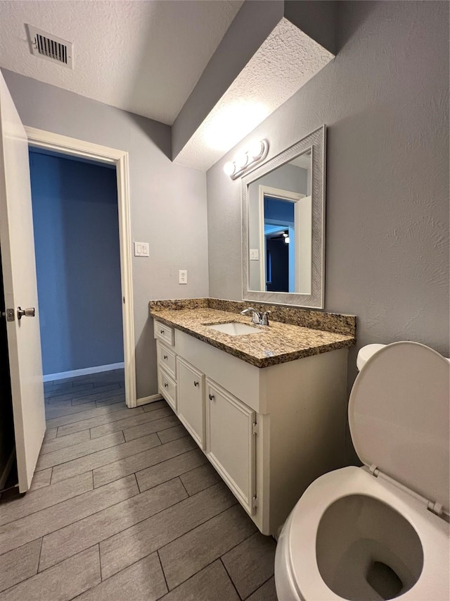 bathroom with a textured ceiling, vanity, and toilet