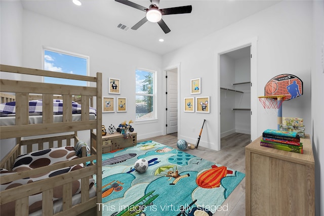 bedroom with light wood-type flooring, a walk in closet, a closet, and ceiling fan