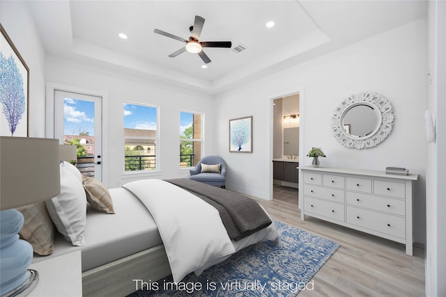 bedroom featuring ceiling fan, light hardwood / wood-style floors, connected bathroom, and a tray ceiling