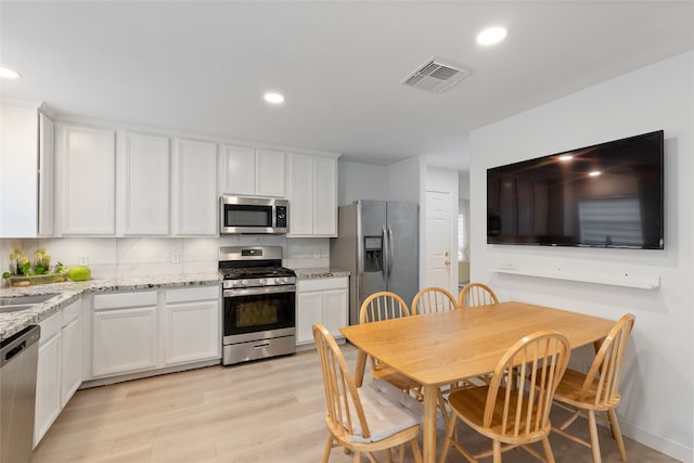 kitchen with light hardwood / wood-style floors, light stone counters, white cabinetry, and appliances with stainless steel finishes