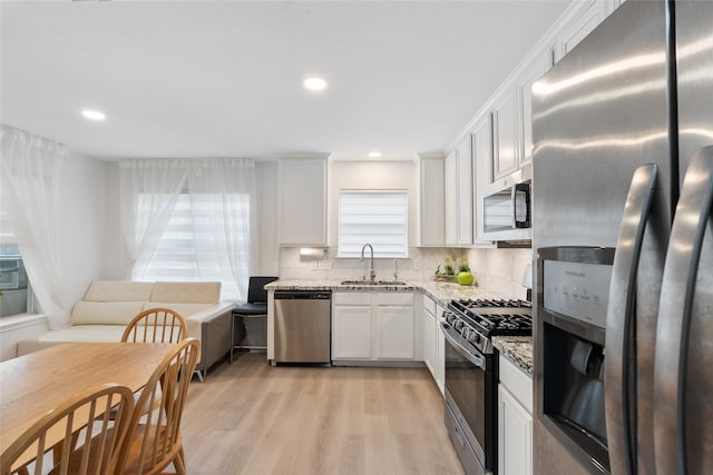 kitchen with sink, light hardwood / wood-style floors, light stone counters, white cabinetry, and stainless steel appliances