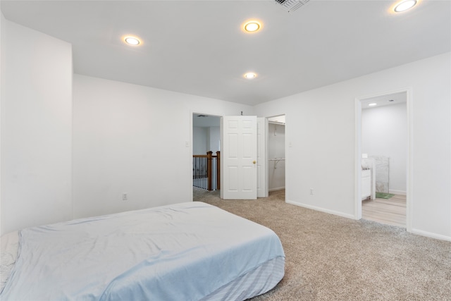 bedroom featuring ensuite bathroom, light colored carpet, and a walk in closet