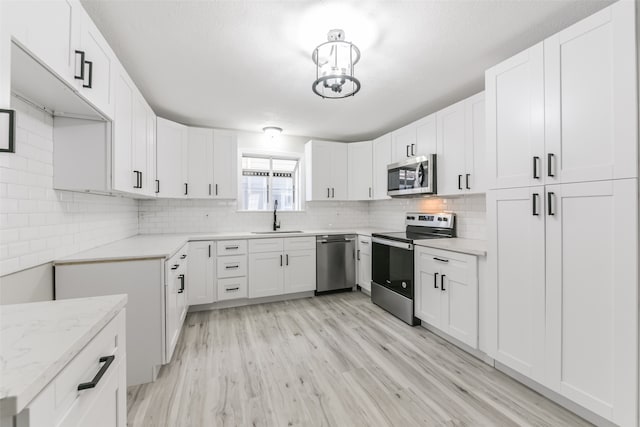 kitchen featuring light stone counters, stainless steel appliances, sink, light hardwood / wood-style flooring, and white cabinets