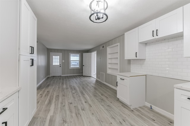 kitchen featuring light wood-type flooring, backsplash, a textured ceiling, an inviting chandelier, and white cabinets