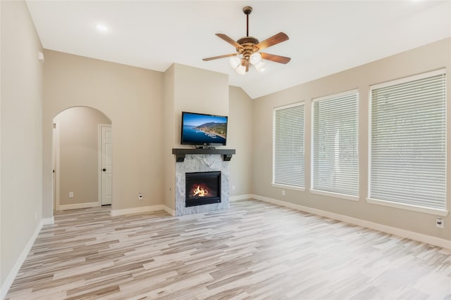 unfurnished living room featuring ceiling fan, light wood-type flooring, a high end fireplace, and vaulted ceiling