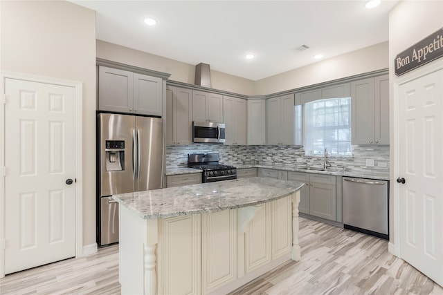 kitchen with a center island, sink, stainless steel appliances, light stone counters, and light hardwood / wood-style flooring