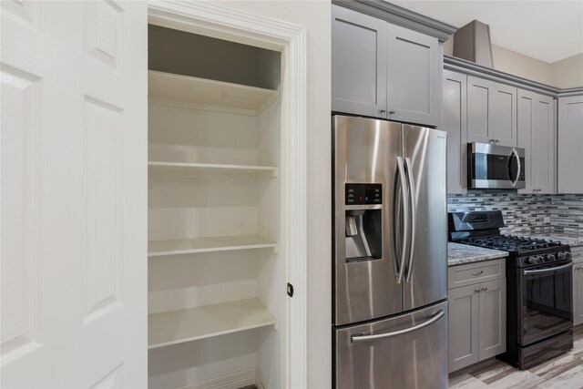 kitchen featuring gray cabinetry, backsplash, light hardwood / wood-style flooring, light stone countertops, and stainless steel appliances