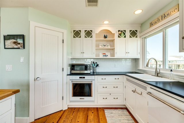 kitchen featuring light wood-type flooring, tasteful backsplash, white appliances, sink, and white cabinetry