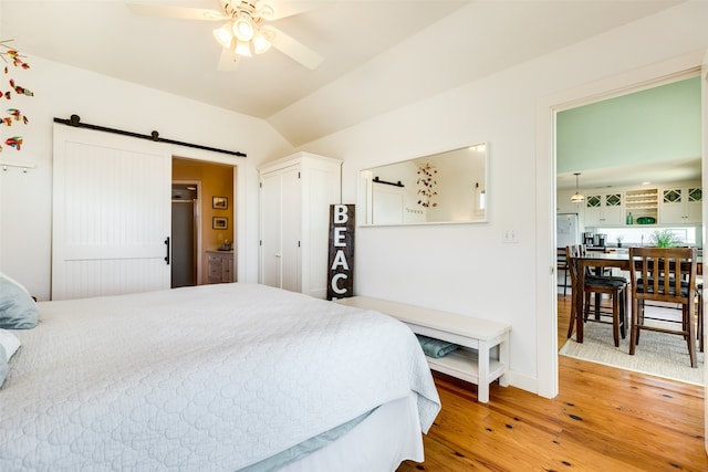 bedroom featuring a barn door, ceiling fan, wood-type flooring, and vaulted ceiling