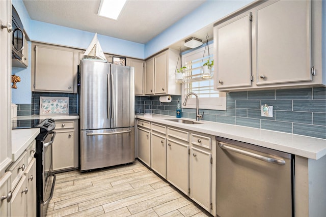 kitchen with gray cabinetry, sink, stainless steel appliances, decorative backsplash, and light wood-type flooring