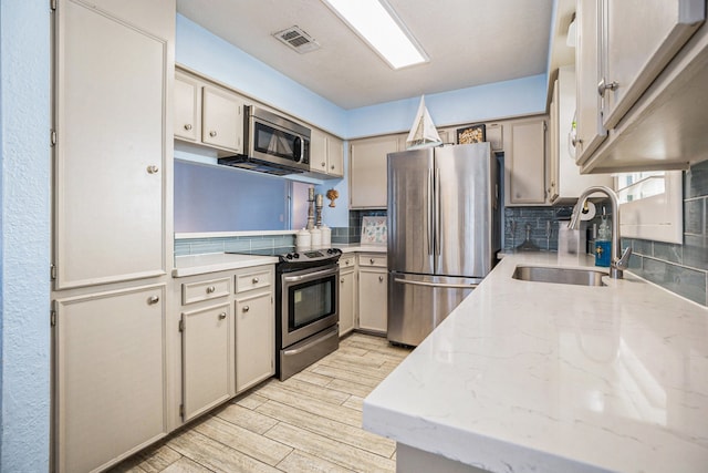 kitchen featuring appliances with stainless steel finishes, tasteful backsplash, light hardwood / wood-style flooring, and sink