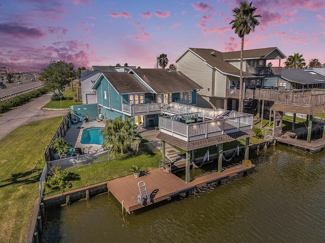 back house at dusk featuring a yard, a swimming pool side deck with water view, a patio, and a balcony