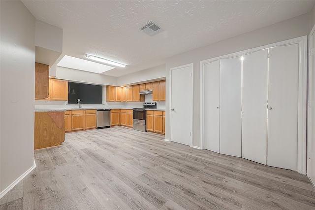 kitchen featuring a textured ceiling, light hardwood / wood-style flooring, stainless steel appliances, and a skylight